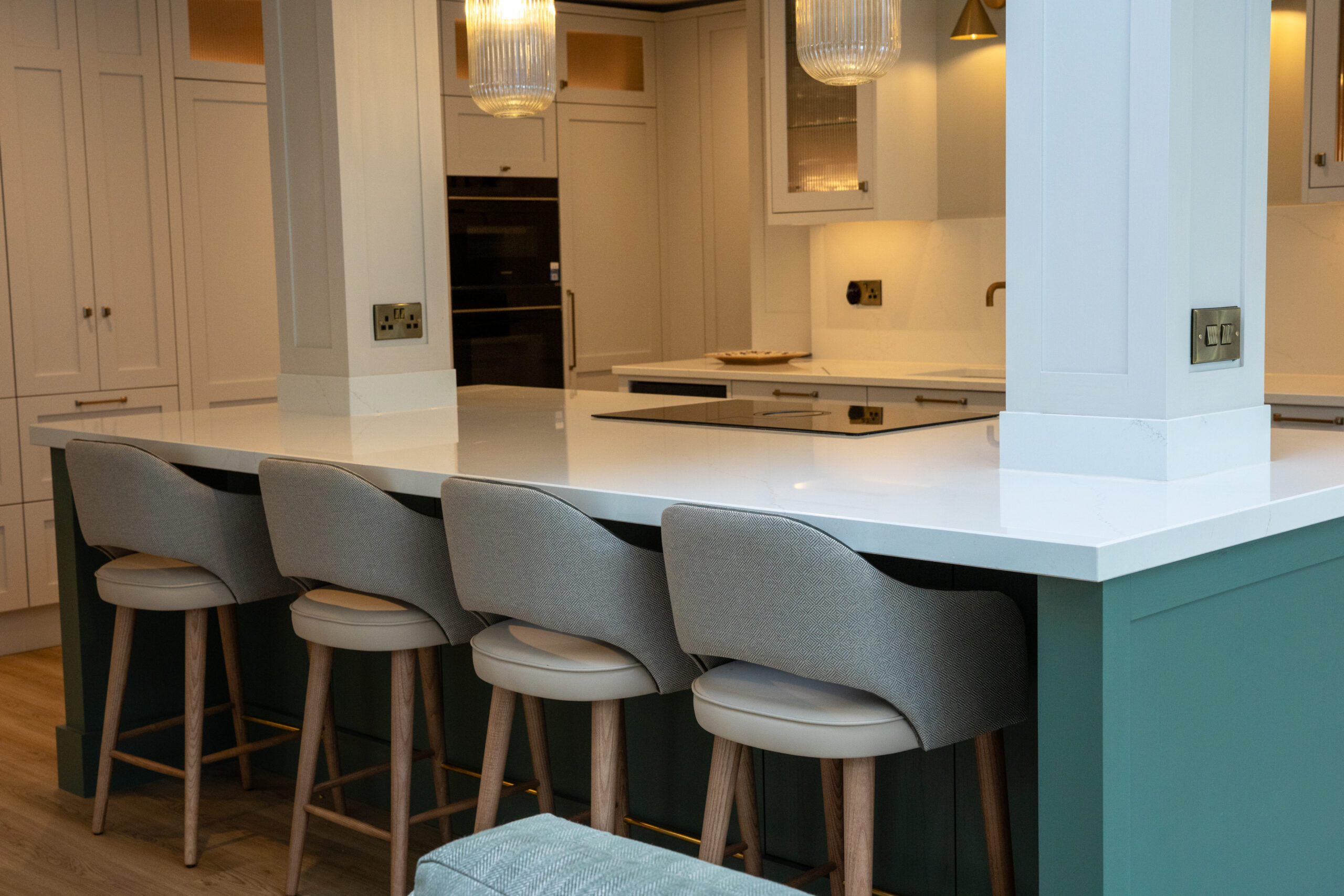Teal island white quartz countertop, grey bar stools, induction hob, shaker kitchen