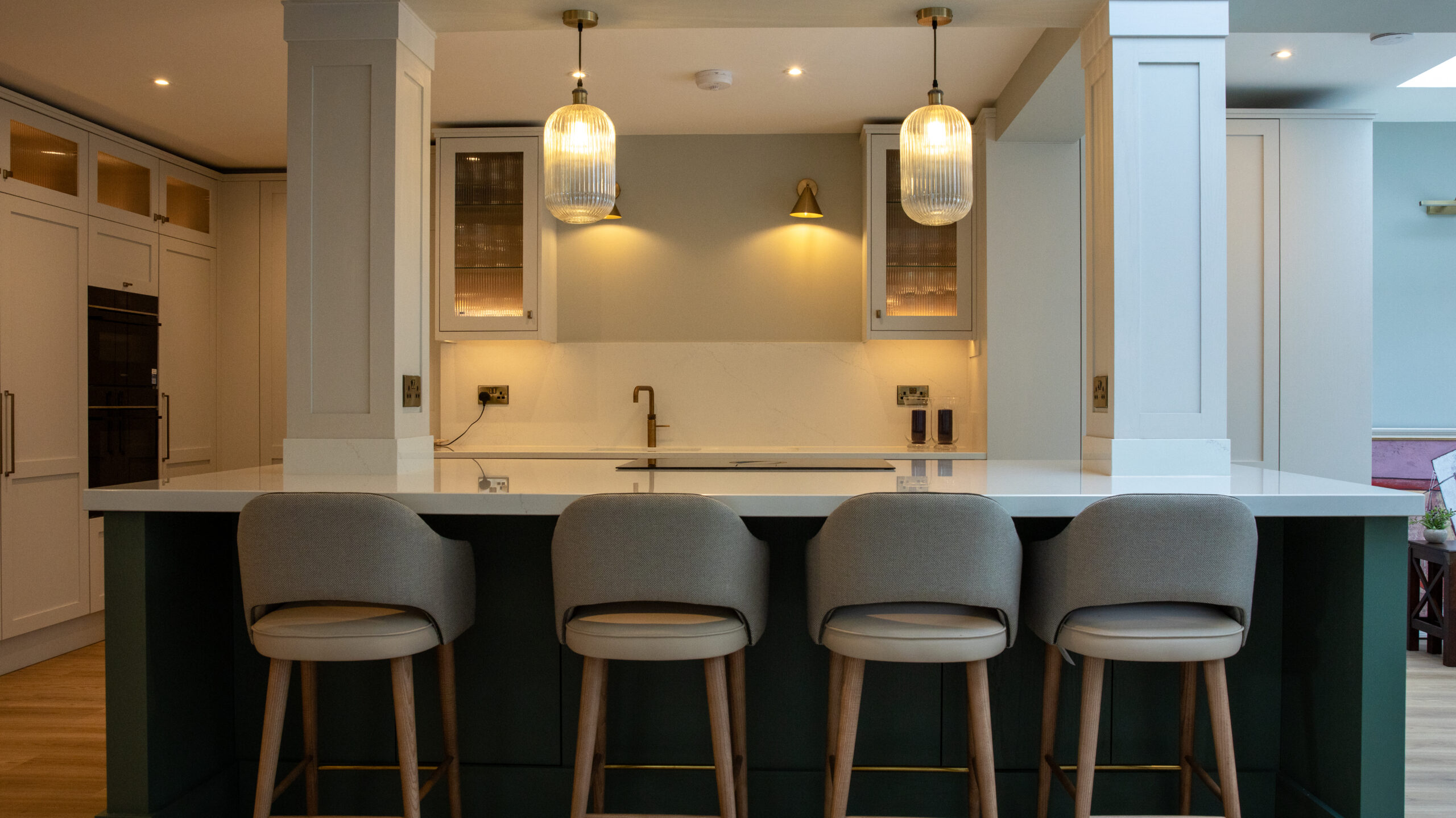 Dark green kitchen island with white quartz countertop and grey upholstered bar stools