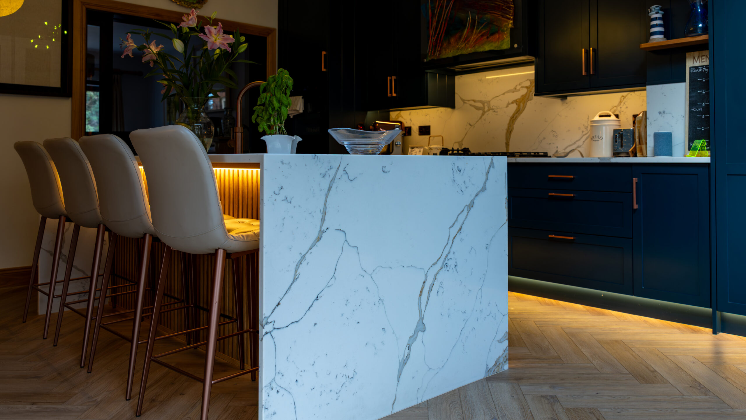 White marble waterfall island with navy blue cabinets and copper bar stools